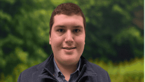 Person smiling outdoors with green foliage background