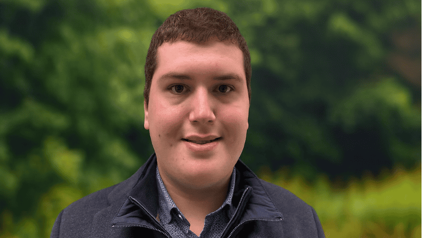 Person smiling outdoors with green foliage background