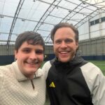 Two men smiling indoors on a football pitch