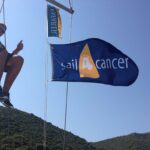 Person sailing with Sail4Cancer flag in sunshine