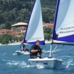 Two people sailing small boats near coastal village