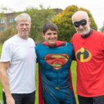 Three men dressed in superhero costumes smiling outdoors