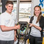 Two people holding a sailing life jacket indoors.